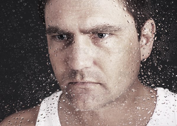 Closeup of pensive man looking through window covered with raindrops