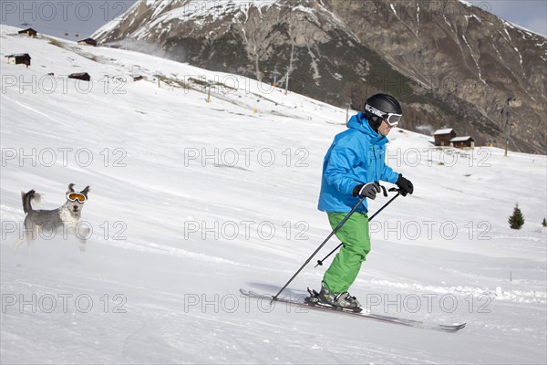 A skier and his dog with snow goggles on a ski slope