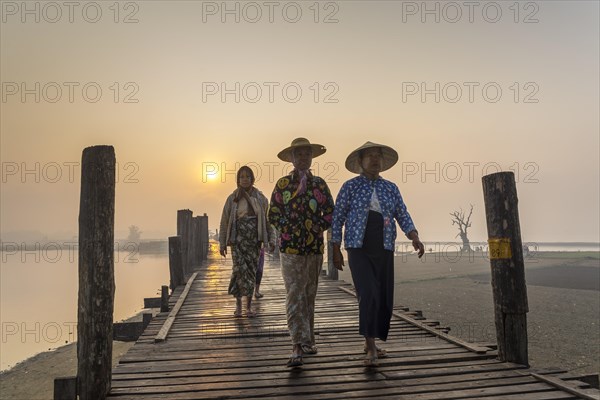 Women wearing traditional hats on a teak bridge