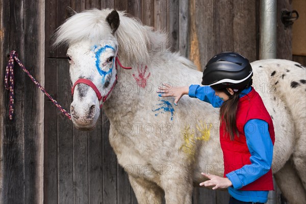 Girl wearing a riding helmet painting a pony with finger paints