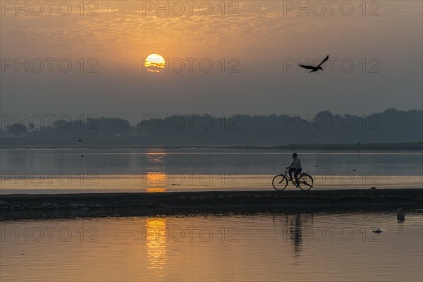 A cyclist crossing the Yamuna river on a dam at sunrise