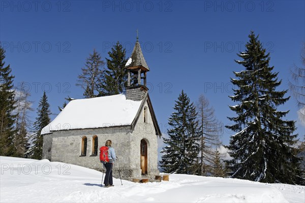 Hiker in winter on the Hemmersuppenalm alpine pasture at St. Anna's Chapel on the way to Fellhorn Mountain