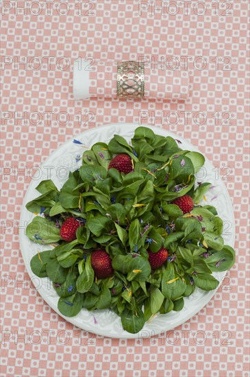 Lamb's lettuce with strawberries and flower petals served on a plate