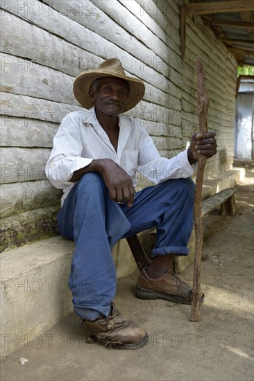 Old man with stick sitting in front of the house