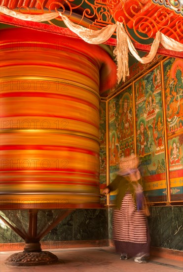 A female devotee spinning a large prayer wheel