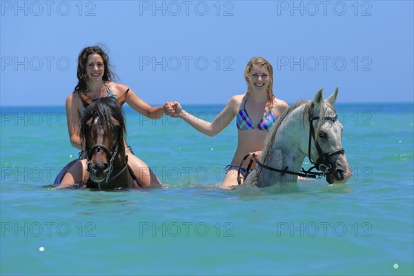 Two women wearing bikinis riding Barb horses in the sea