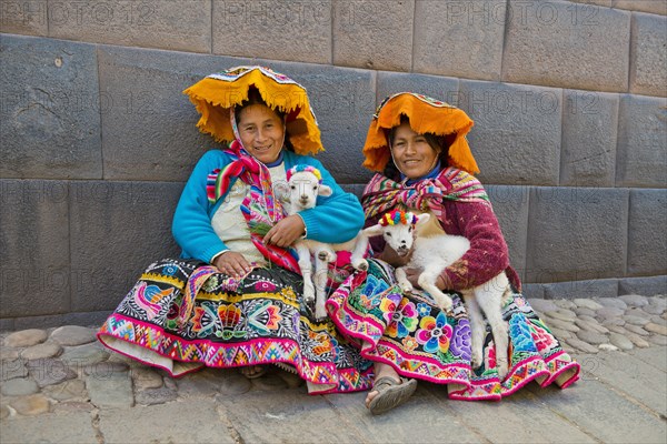 Two Quechua women in traditional dress holding lambs in their arms