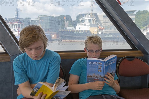 Young people on a language trip read an English travel guide on the Elbe ferry