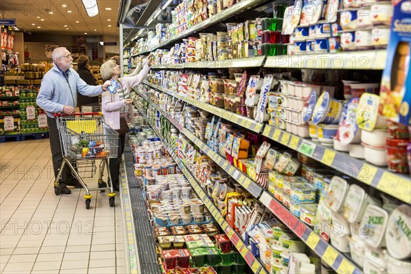 Senior couple shopping with a shopping trolley in the refrigerated dairy section in a supermarket