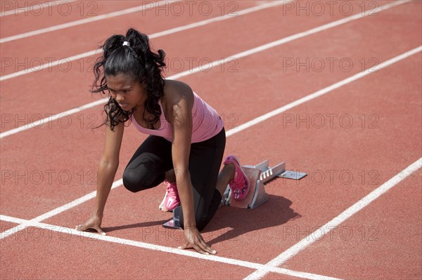 Sporty young woman in starting position on starting blocks