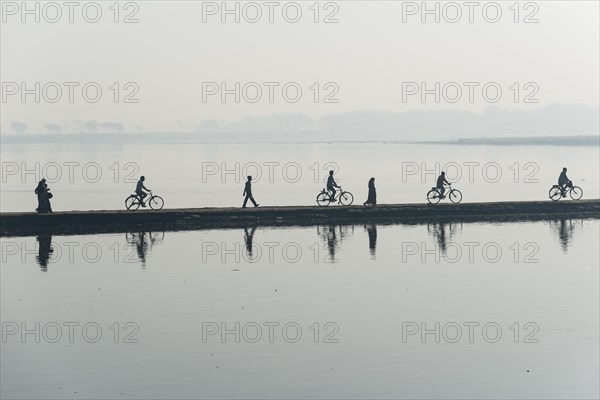 Cyclists and pedestrians crossing the Yamuna river on a dam in the morning