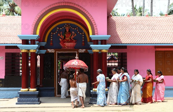 A group of women with offerings and a priest circling a Hindu temple