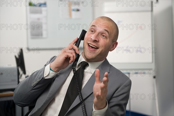 Young man wearing a suit is talking on a phone in the office