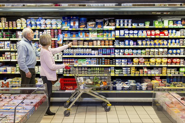 Senior couple shopping with a shopping trolley in the refrigerated dairy section in a supermarket