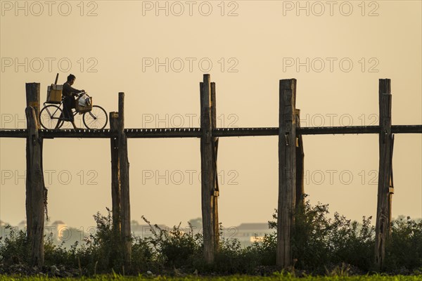 Man with a bike walking on a teak bridge