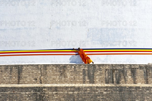Monk tying a cloth around a large white stupa