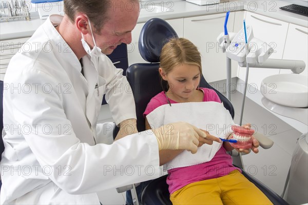 Dentist showing a girl the proper use of a toothbrush