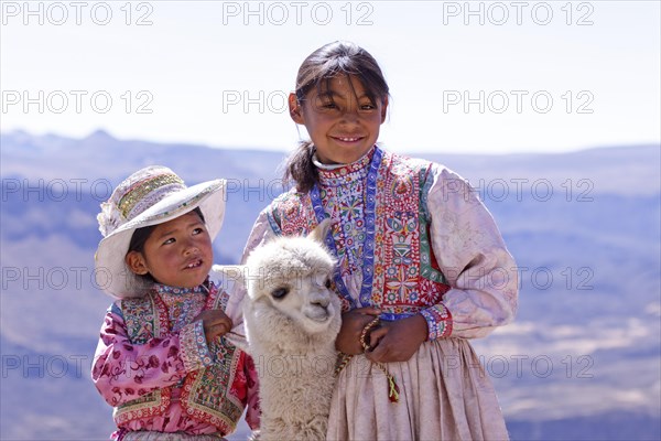 Two girls in traditional dress with an alpaca