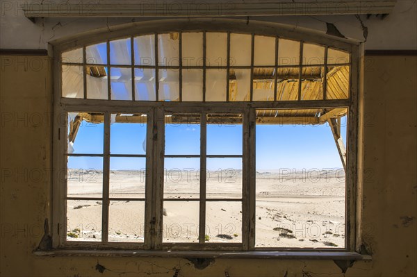 View through a window of an abandoned house in a former diamond miners settlement that is slowly covered by the sand of the Namib Desert