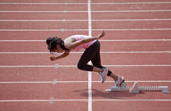 Sporty young woman starting from starting block to run on running track