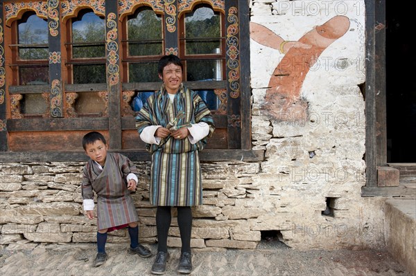 Father and son standing in front of house wall with the mural of a phallus