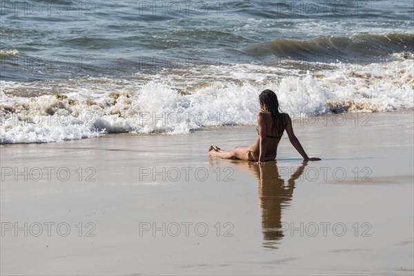 A young woman wearing bikini is sitting in the sand of Anjuna Beach
