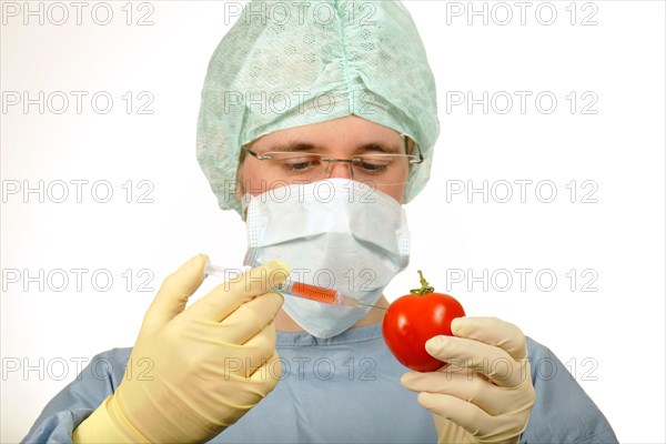 Chemist in sterile scrubs holding a syringe and a tomato