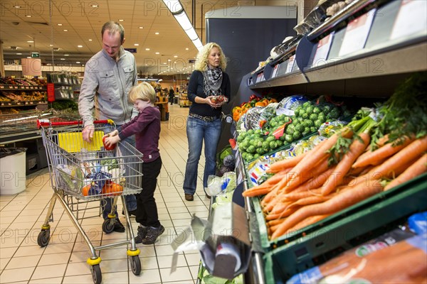 Family shopping with a shopping trolley in the fruit and vegetables department of a supermarket