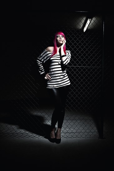 Woman with pink hair in front of a chain link fence