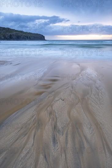 Water flows via bizarre structures on the sandy beach into the sea