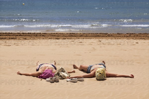 Two women with covered heads sunbathing on the beach