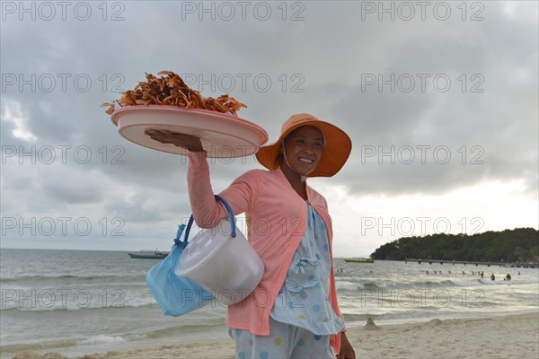 Young Cambodian woman wearing a sun hat selling crabs and shrimps on the beach