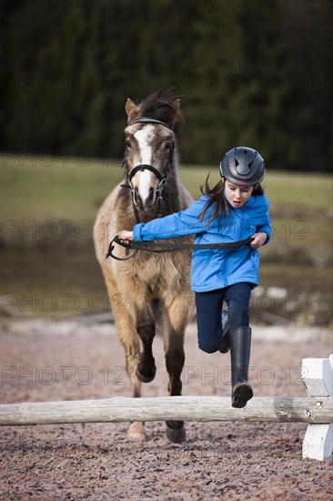 Girl wearing a riding helmet jumping over an obstacle with a pony