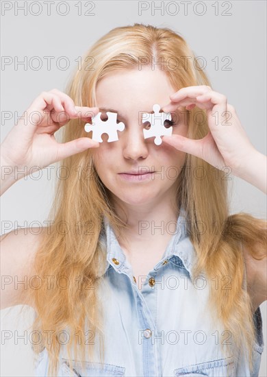 Woman holding two white puzzle pieces in front of her eyes