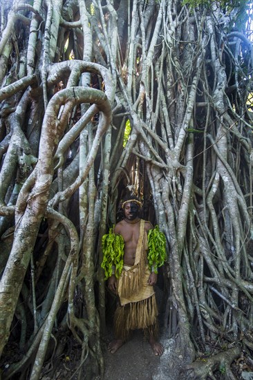 Traditional dressed man with black face standing in a giant banyon tree