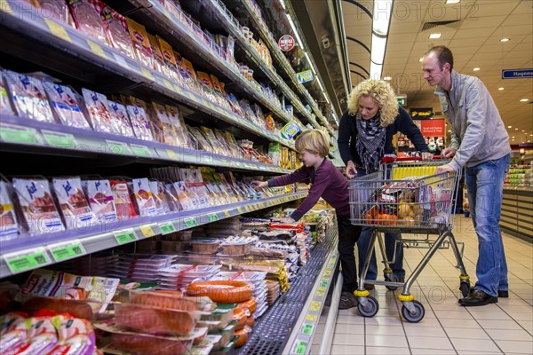 Family shopping with a shopping trolley in the refrigerated section of a supermarket with packed meat