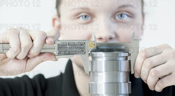 A female cutting machine operator trainee is measuring a casing with a caliper