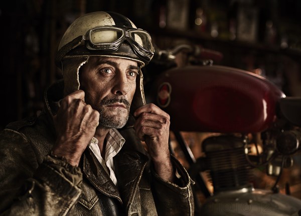 Man with old leather jacket putting on an old motorcycle helmet