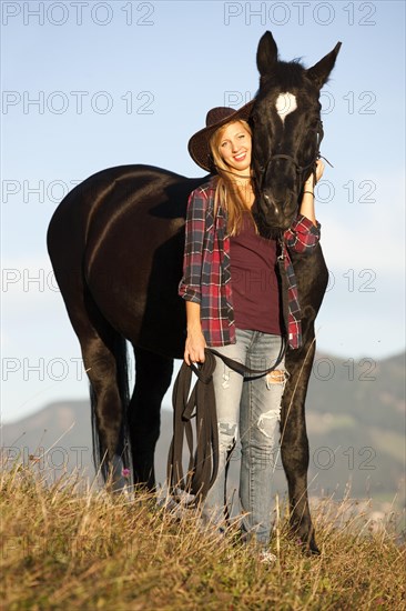 A young woman and a black Hanoverian horse standing on a mountain meadow in autumn