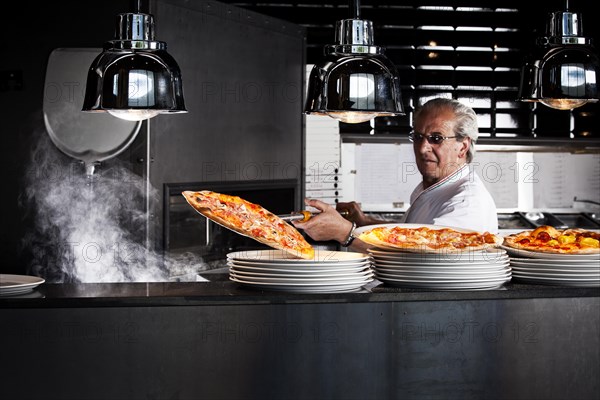 Pizza baker taking the finished pizza out of the oven with a pizza shovel