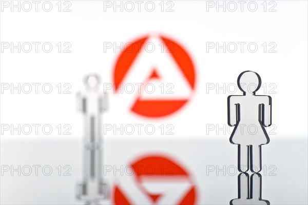 Two figures standing in front of the logo of the German employment agency