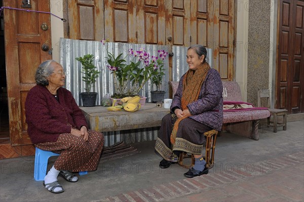 Lao women wearing typical sarongs sitting in front of a house