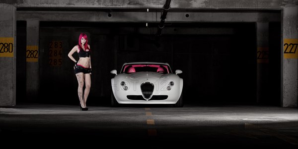 Woman with pink hair and tattoos standing next to a white sports car