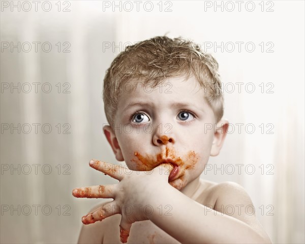 Toddler licking tomato sauce off his thumb