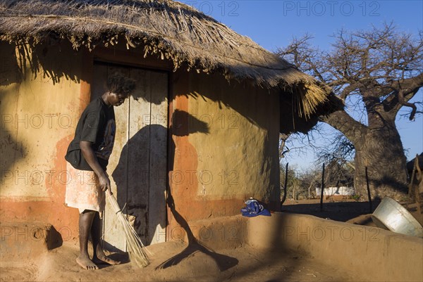 Woman sweeping in front of adobe house