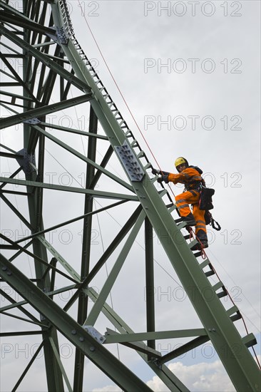 Overhead transmission cable installer climbing a mast to install insulated cable on a newly built high-voltage transmission mast