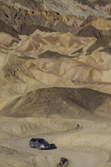 Car driving on the road through the badlands of the 'Twenty Mule Team Canyon' in the morning light