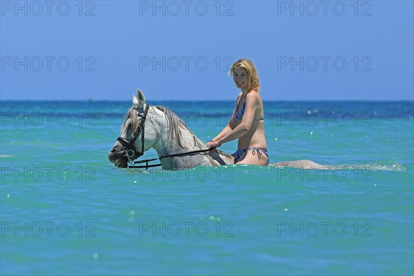 Woman wearing a bikini riding a Barb horse in the sea