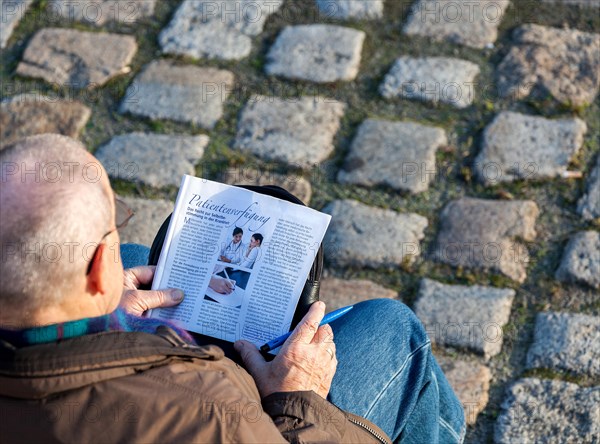 Senior citizen sitting on a bench studying a brochure for making a 'Patientenverfugung'