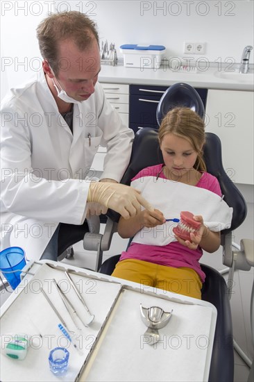 Dentist showing a girl the proper use of a toothbrush